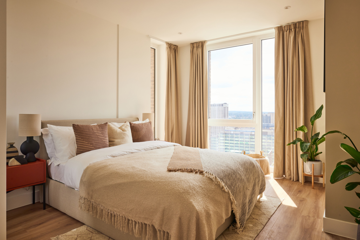 A modern bedroom in neutral tones, with floor-to-ceiling windows looking over a cityscape